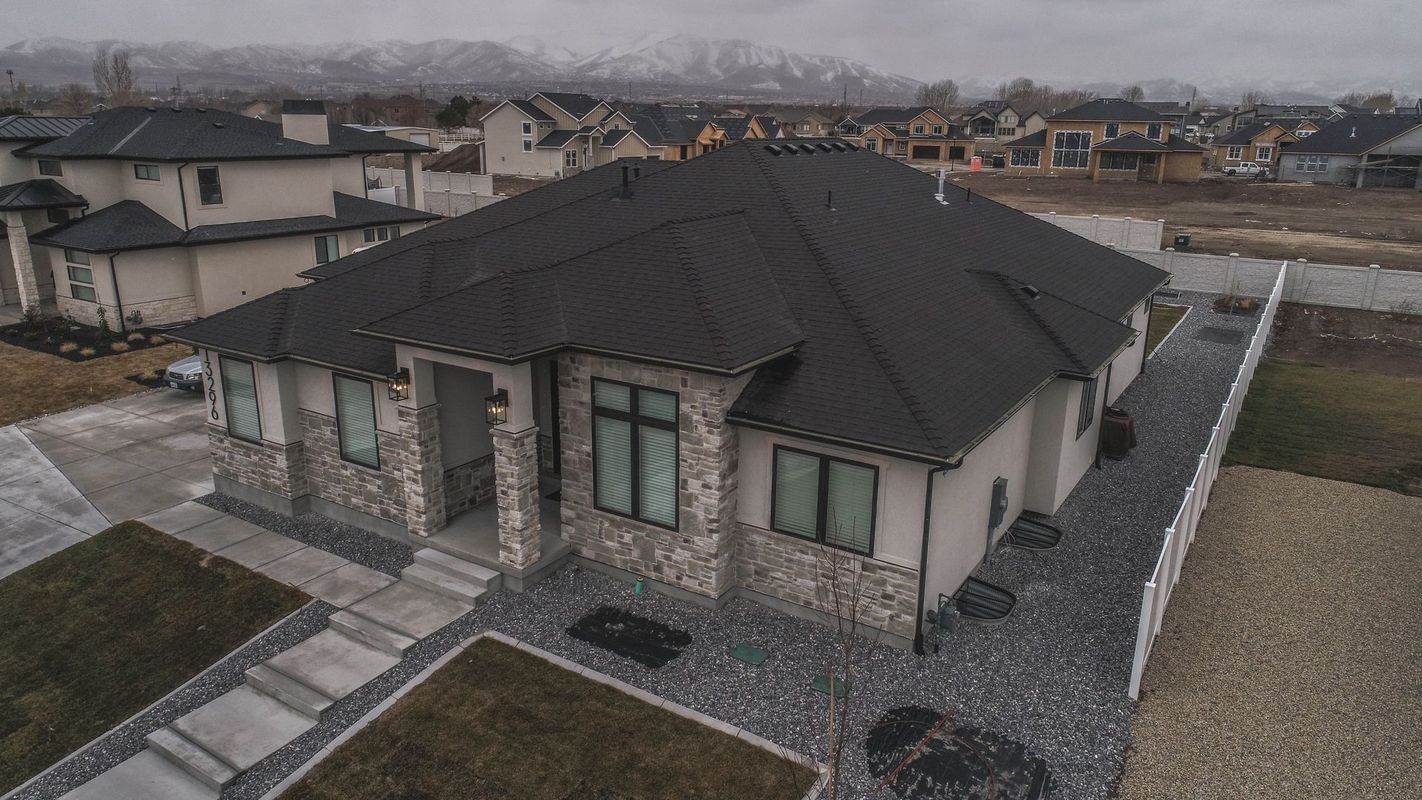 An aerial view of a house with a black roof in a residential area.