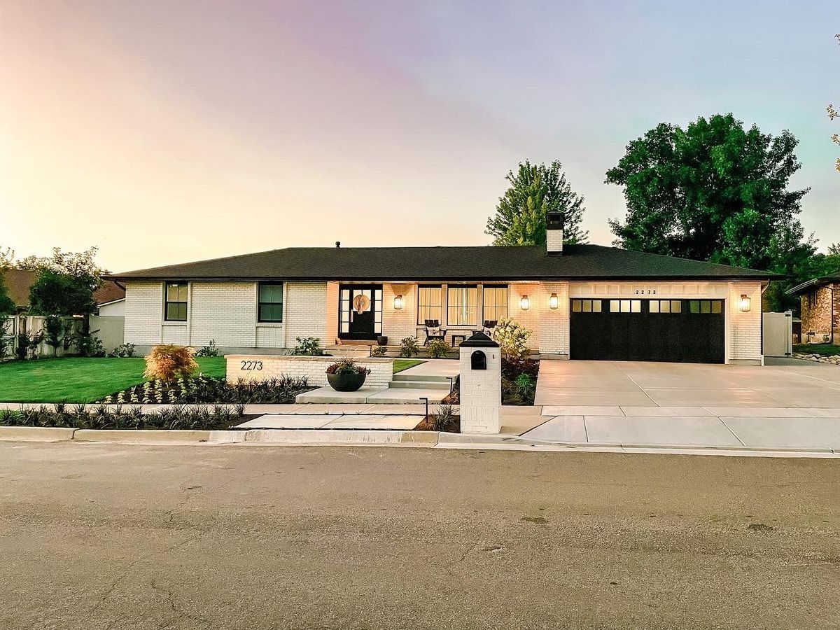 A white house with a black garage door is sitting on the side of the road.