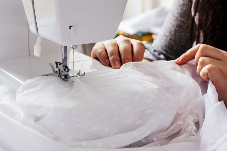 Woman sewing white fabric with a sewing machine, indoor setting.
