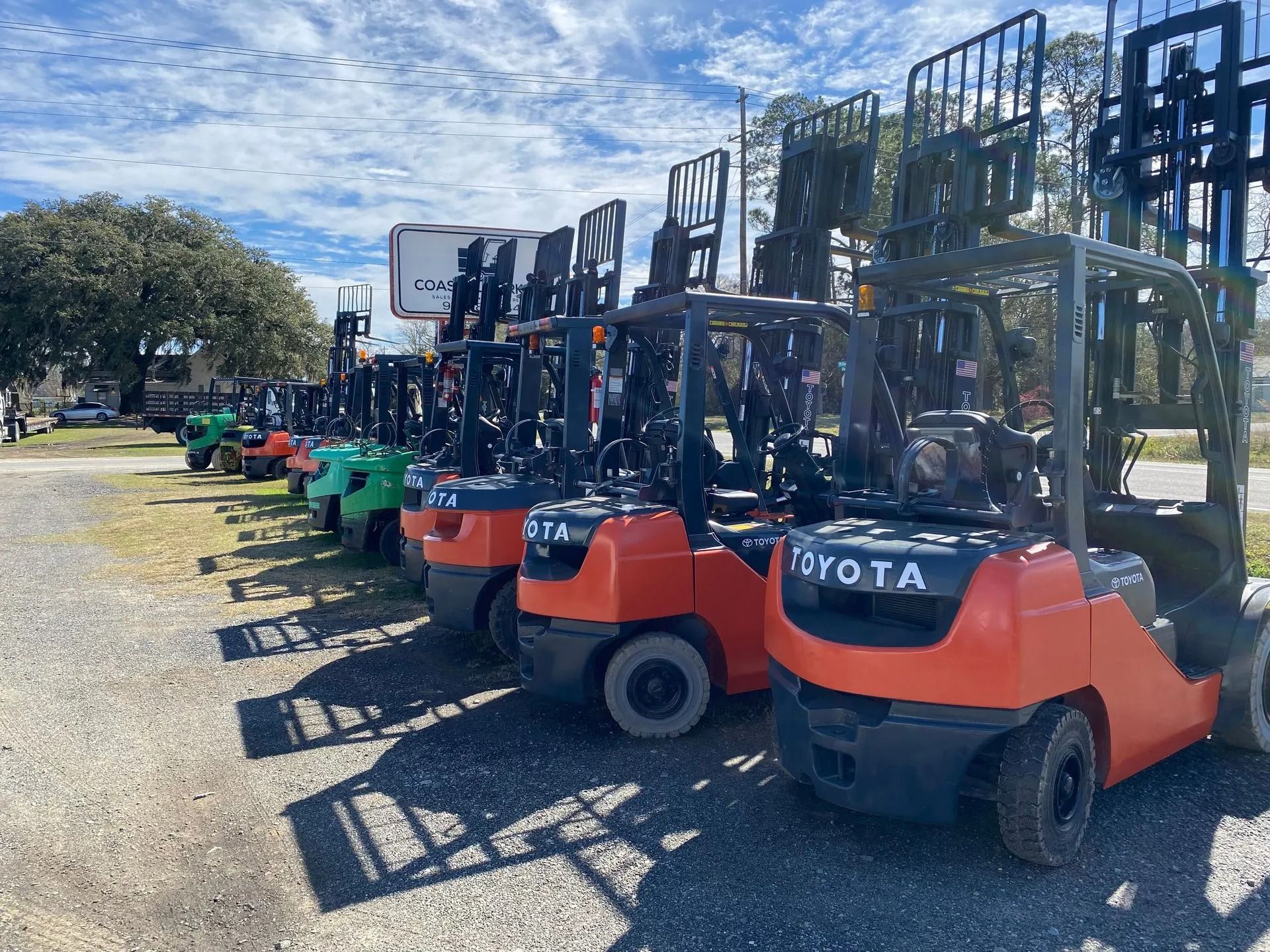 Row of orange, green, and red forklifts parked outside on a sunny day.