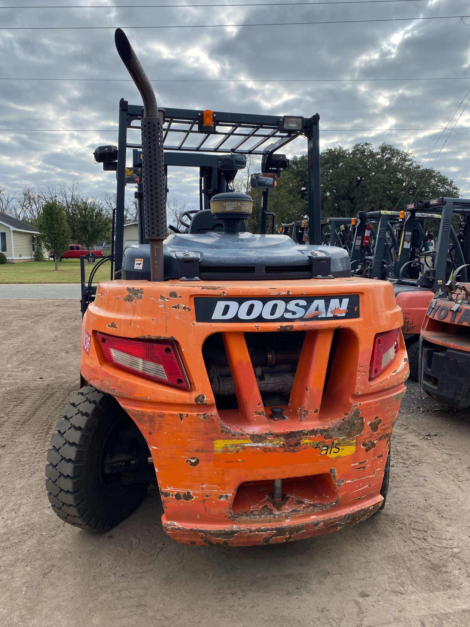 Orange Doosan forklift outdoors; weathered paint, black wheels, exhaust stack.