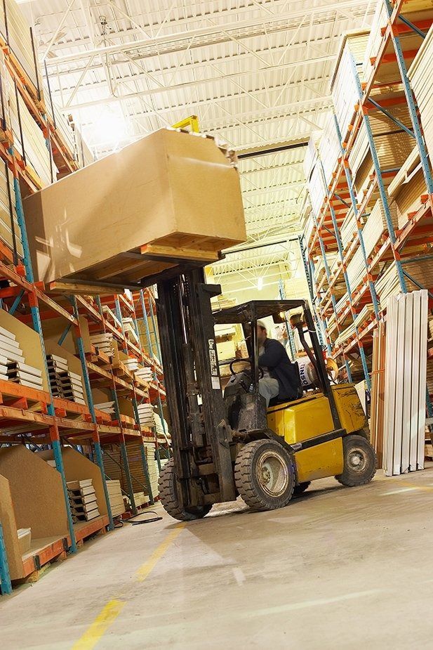 Forklift lifting a large cardboard box in a warehouse, worker driving.