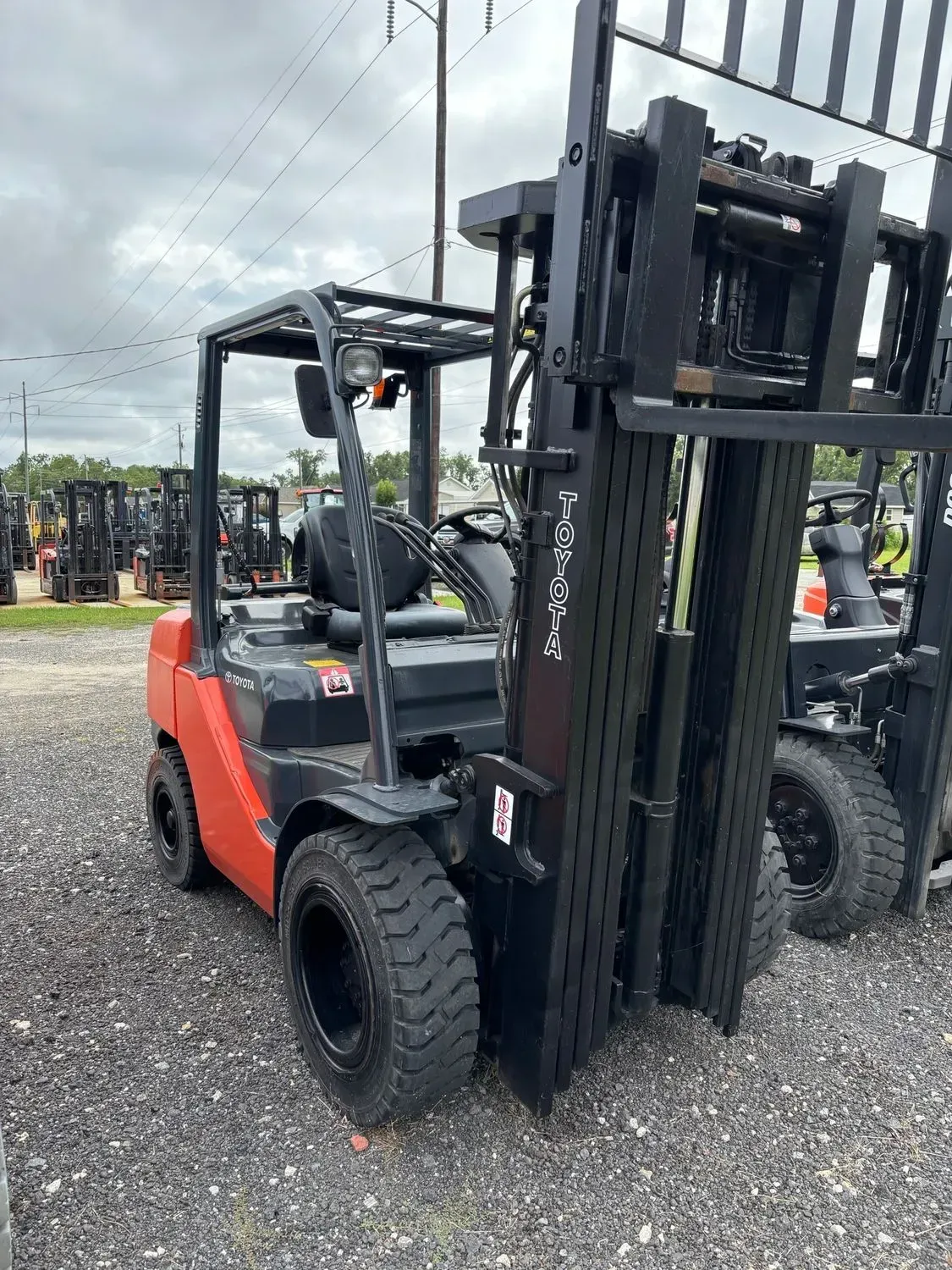 Orange and black forklift on gravel lot; other forklifts in background.