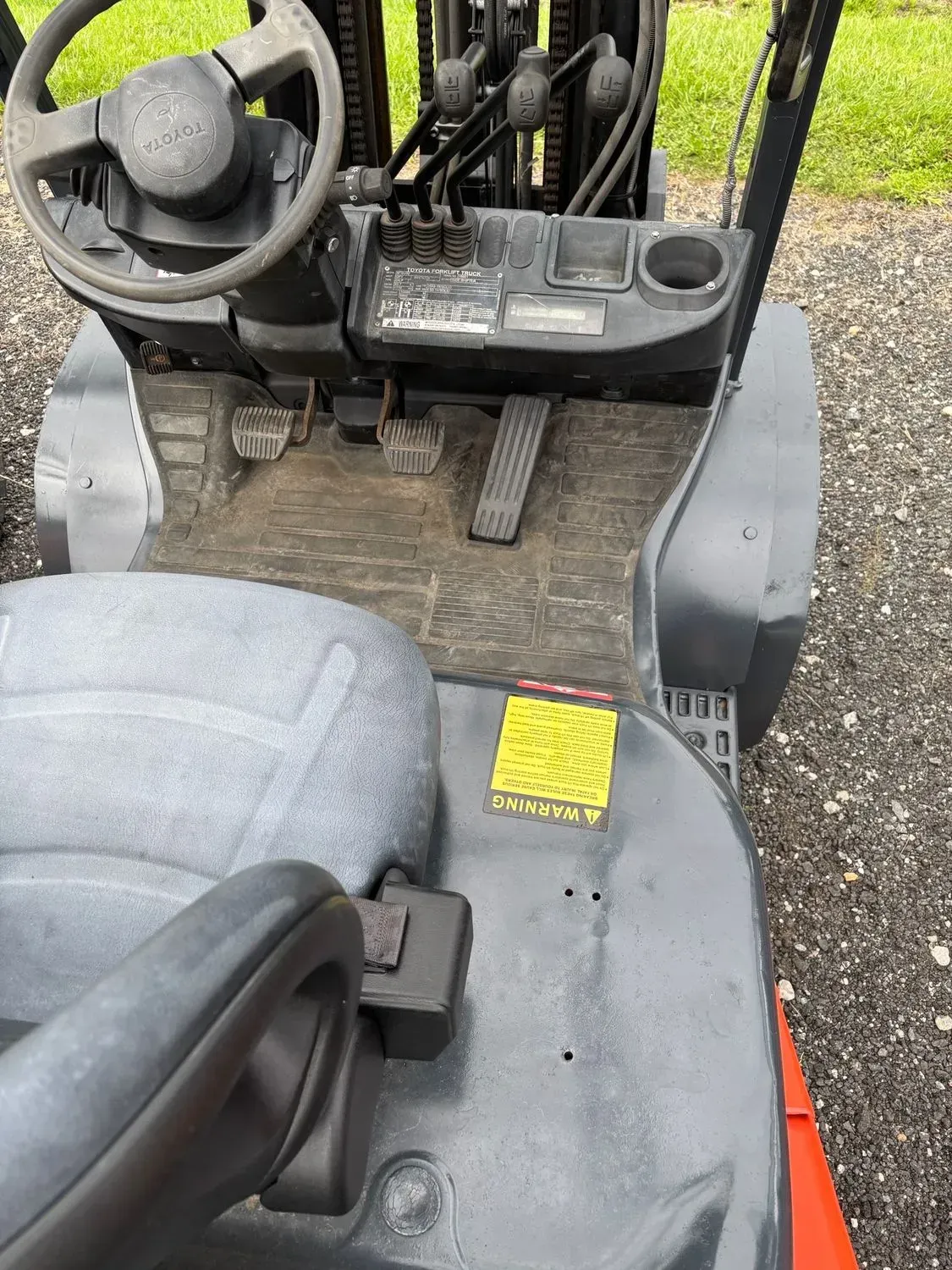 Interior of a forklift showing steering wheel, pedals, controls, seat, and cup holder.