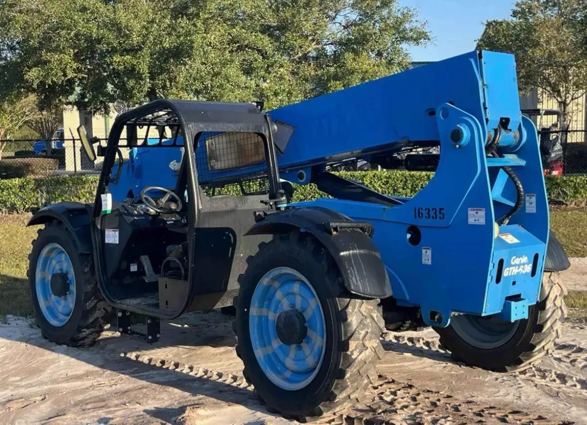 Blue Genie telehandler on a dirt surface. The boom is extended. Sunny outdoor setting.