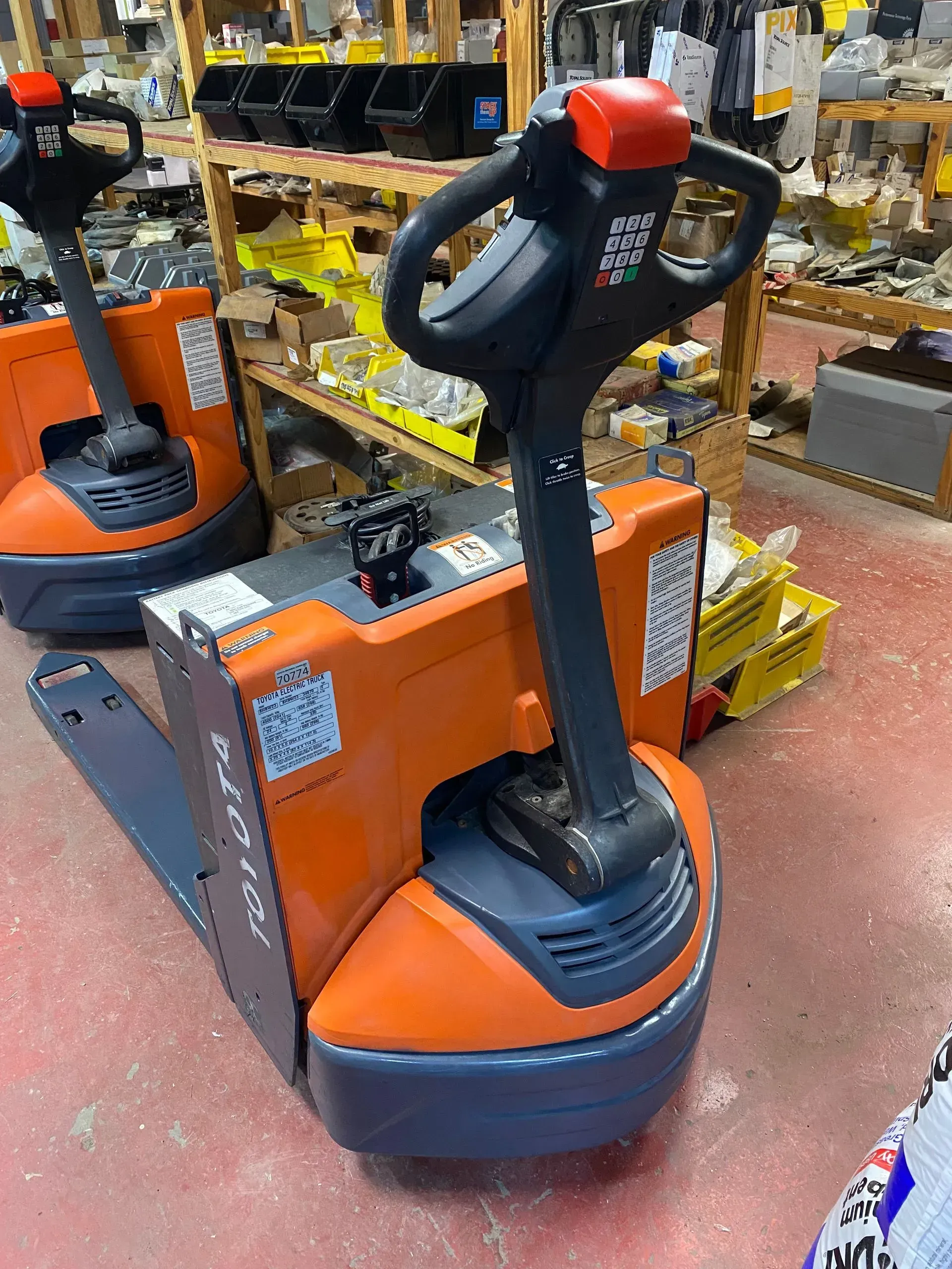 Orange and gray electric pallet jack in warehouse setting.