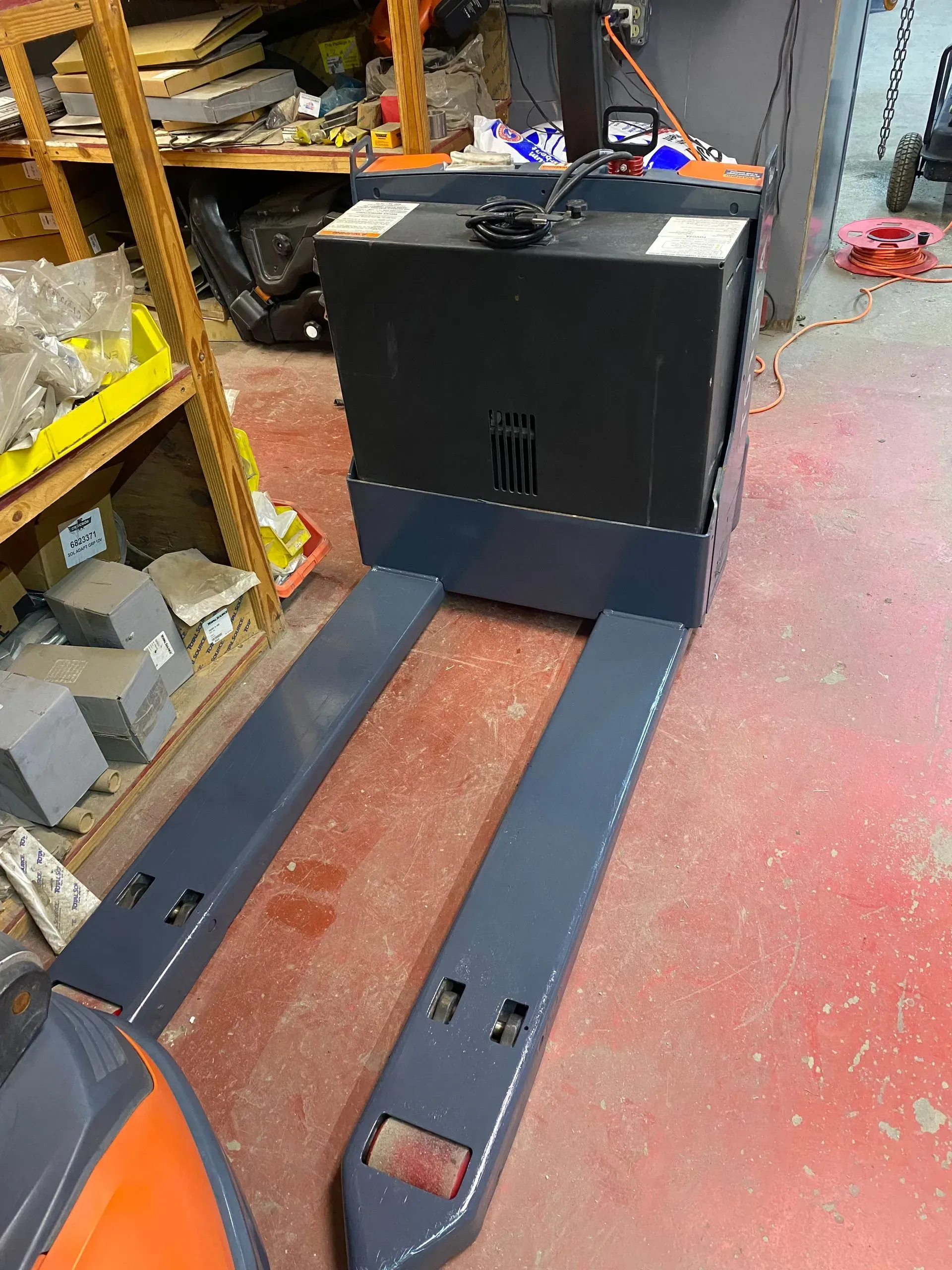 Electric pallet jack in a warehouse with a dark grey body and silver forks.