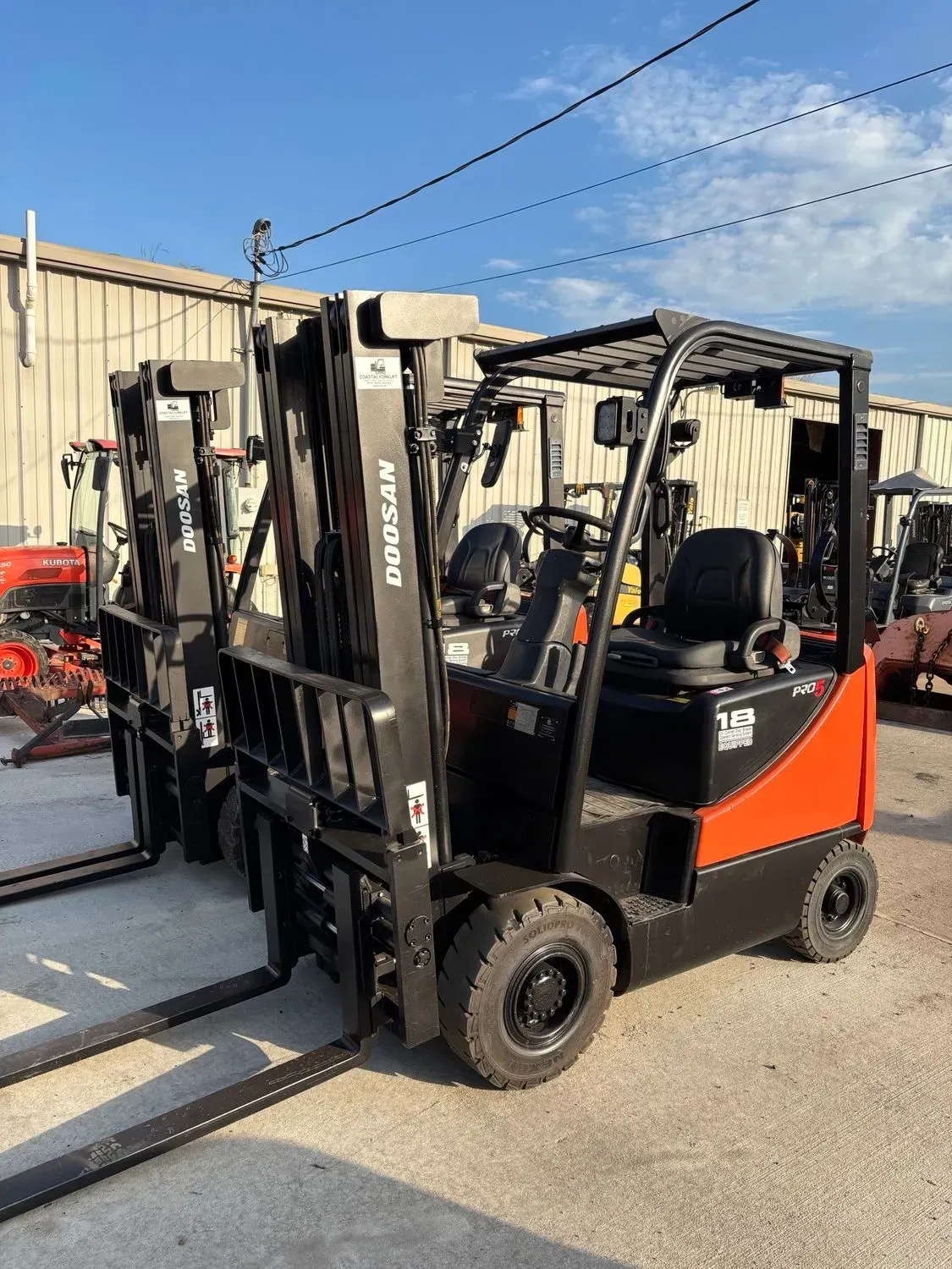 Orange and black forklift truck in front of a metal building on a sunny day.