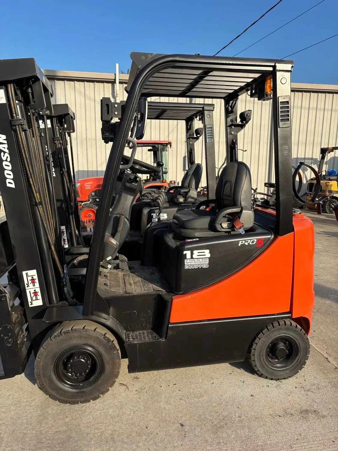 Orange and black Doosan forklift with a protective overhead cage, parked outdoors.