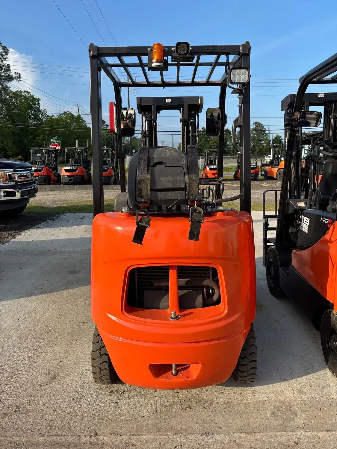 Orange forklift on a gravel lot, other forklifts in background.