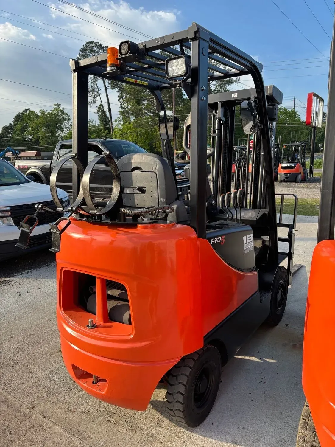 Orange and black forklift outdoors, next to other vehicles, under a cloudy sky.