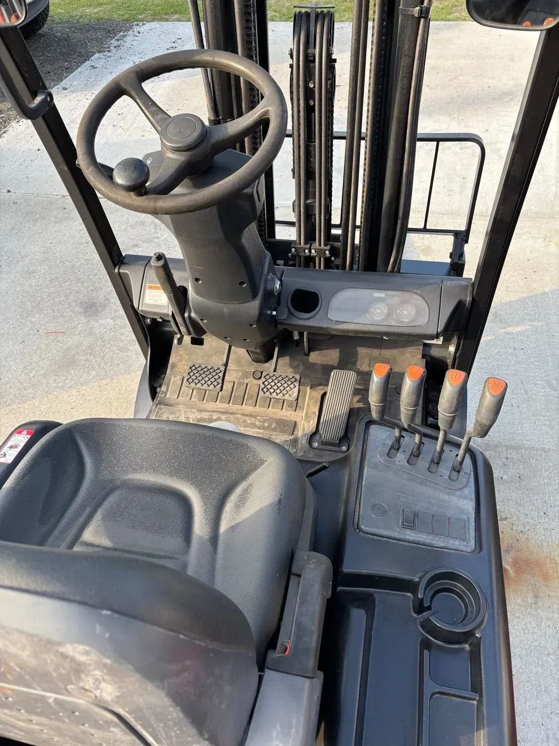 Interior view of a black forklift showing the seat, steering wheel, levers, and pedals.
