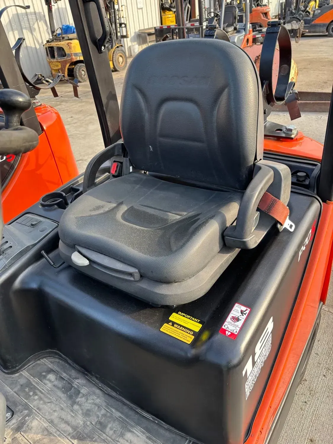 Black forklift seat with seatbelt in an outdoor setting.