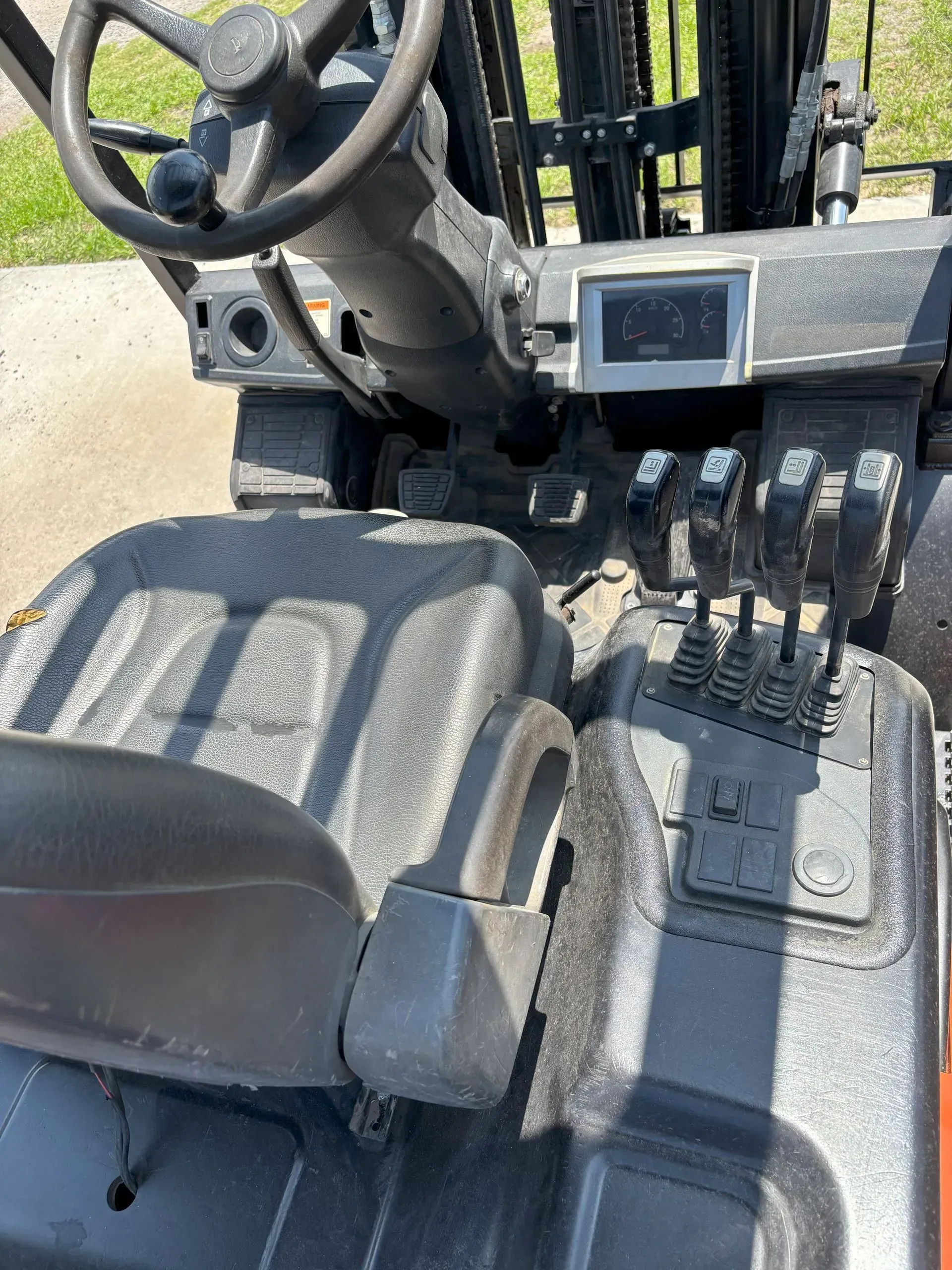 Interior of a forklift with a seat, steering wheel, display screen, and control levers.