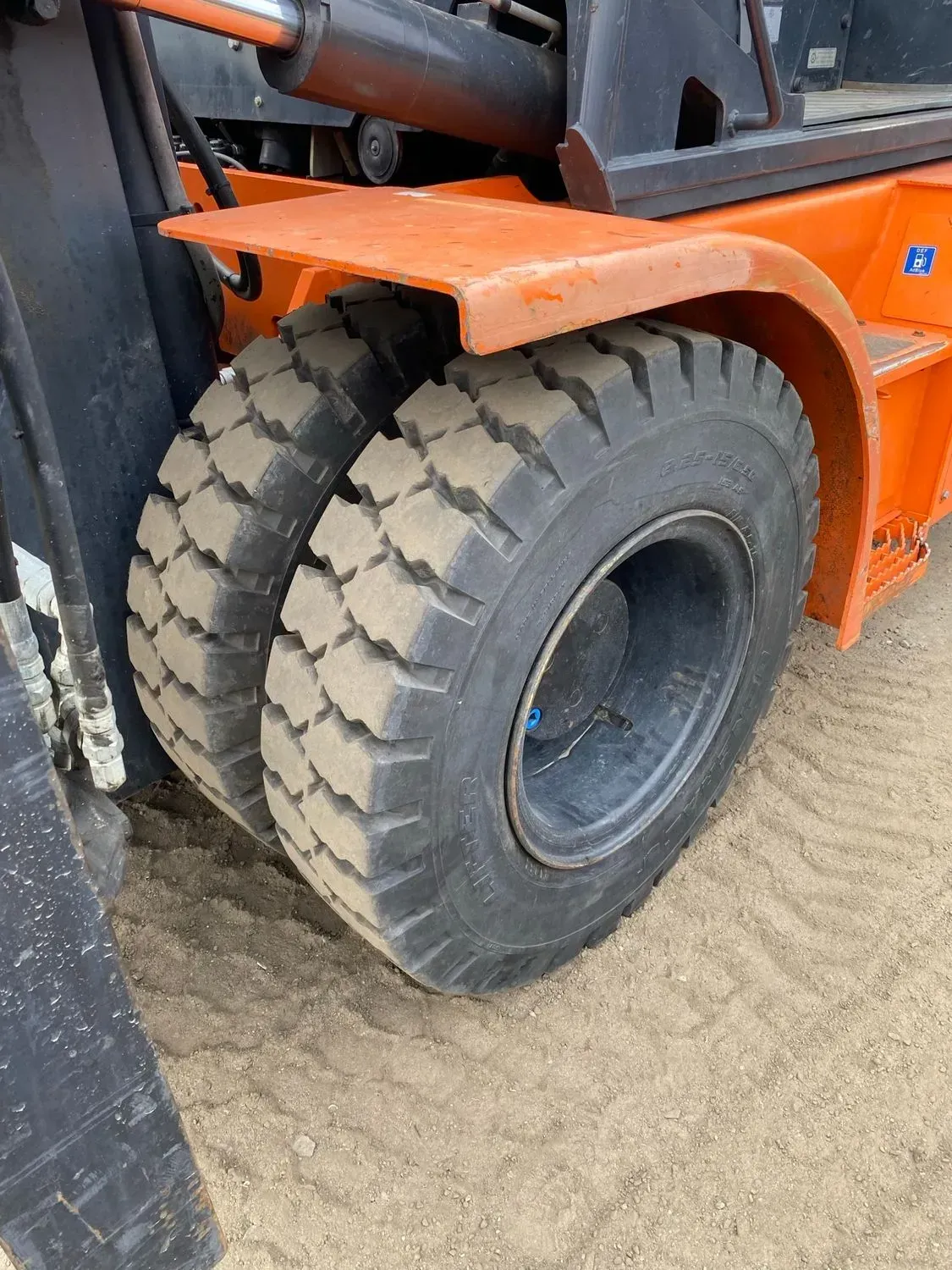 Orange forklift with two black tires on a dirt surface.