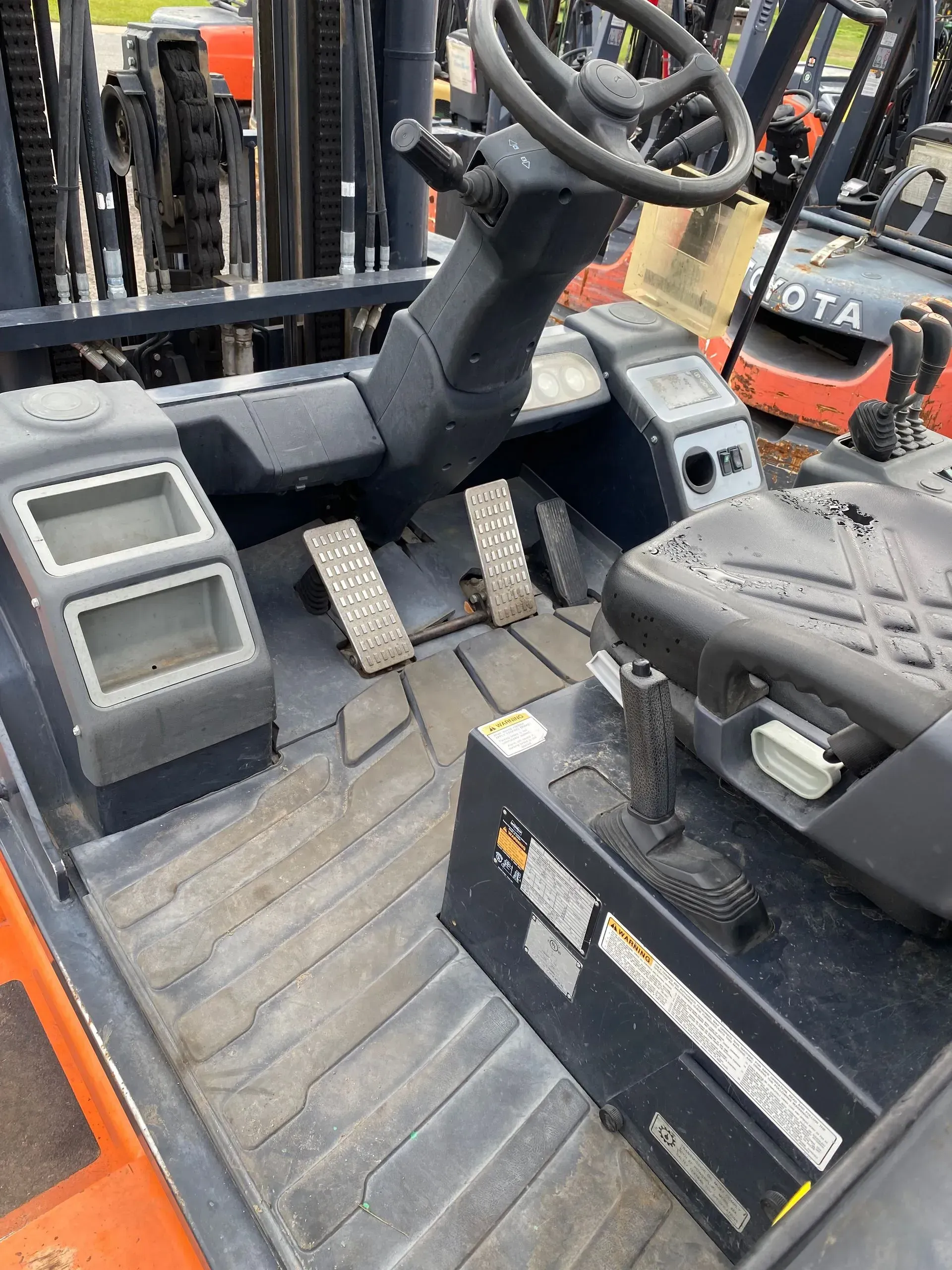 Interior view of an orange forklift cab with a steering wheel, pedals, and gauges.