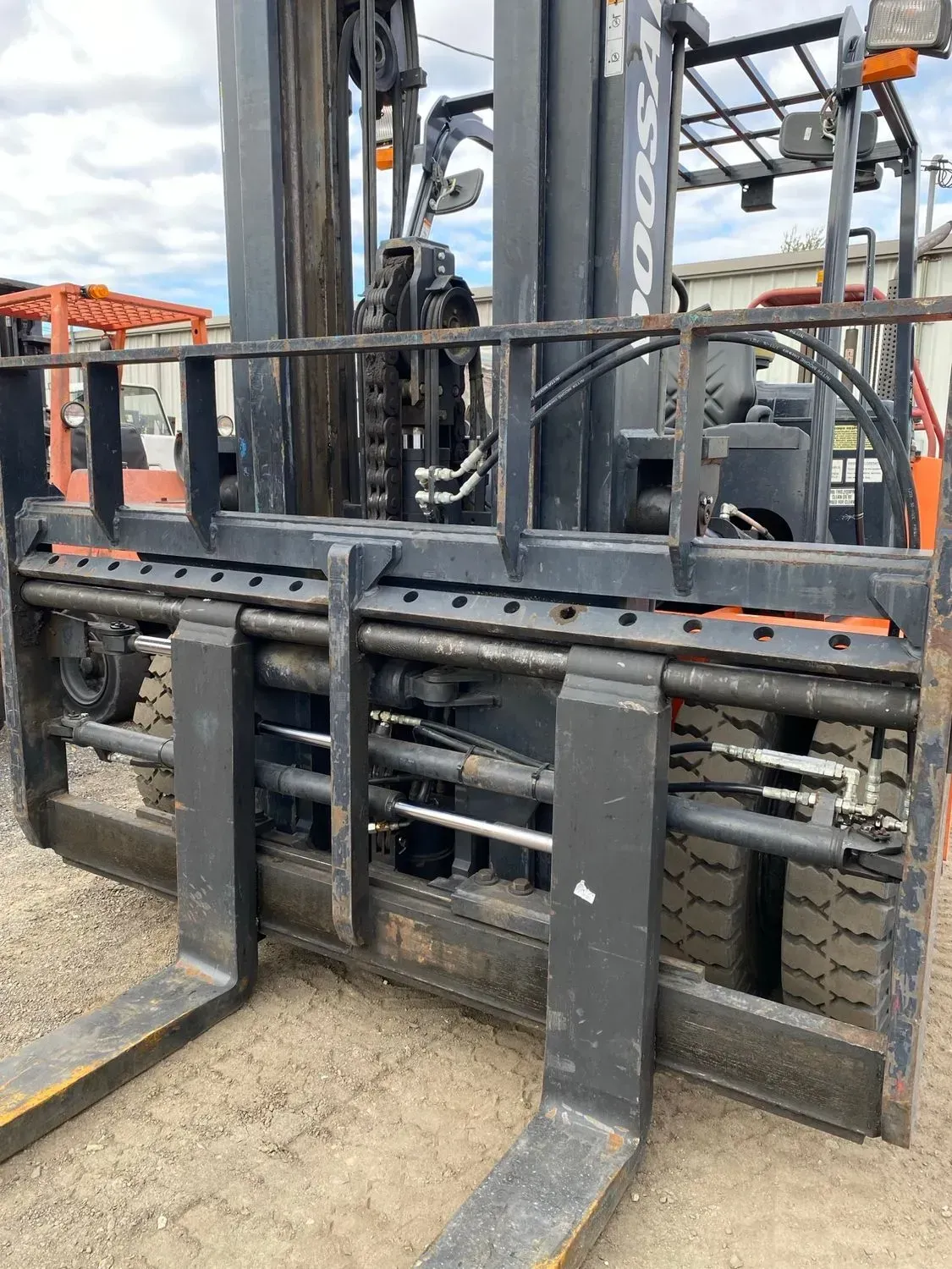 Forklift with black forks, orange frame, and black tires, outdoors.