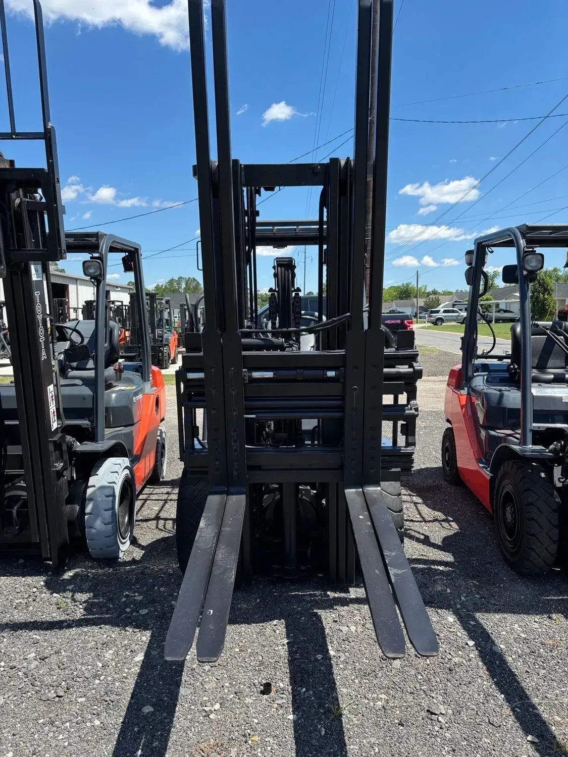 Forklift, front view, black and orange, on a paved lot on a sunny day.