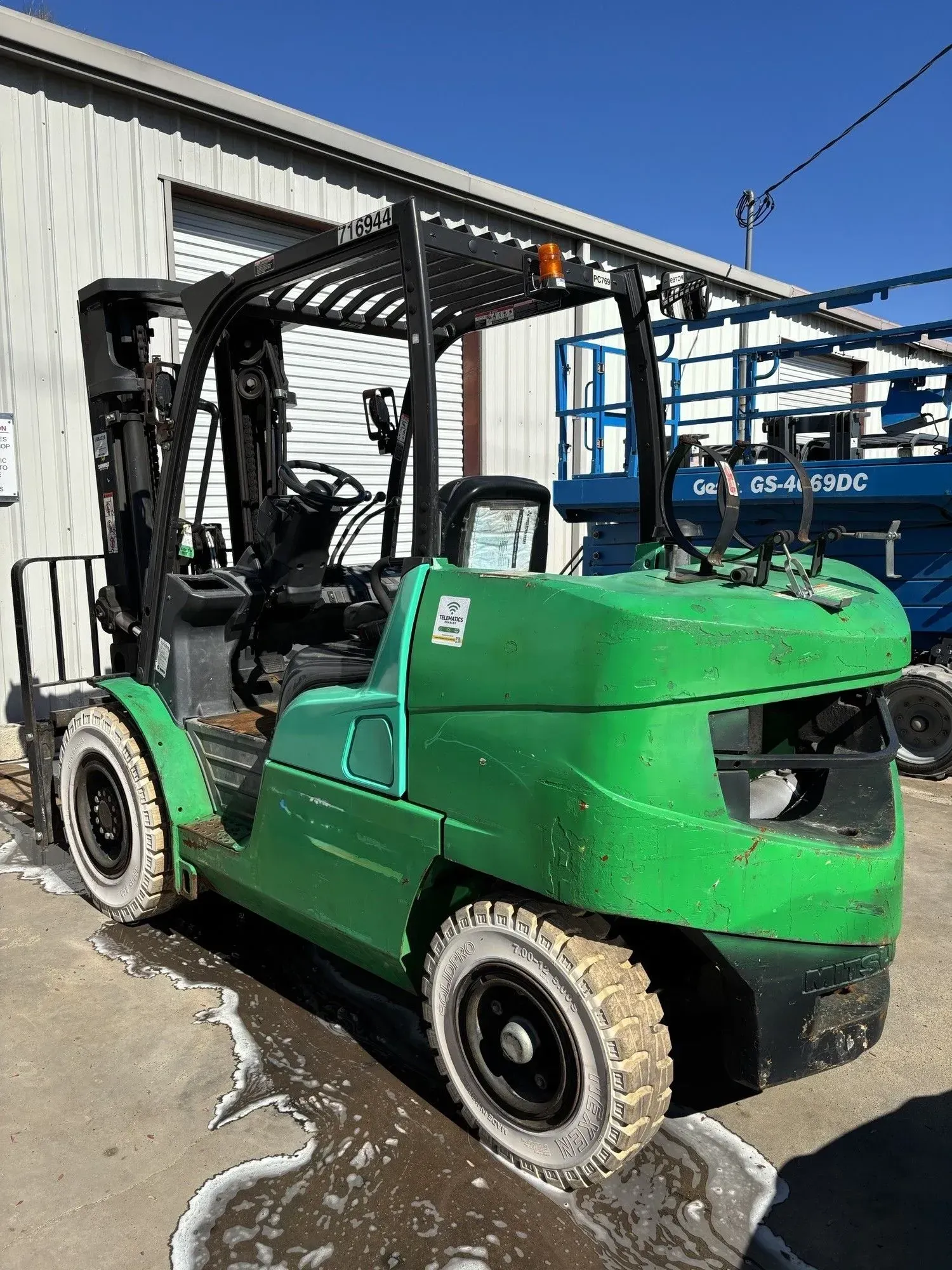 Green forklift with white tires parked in front of a building.