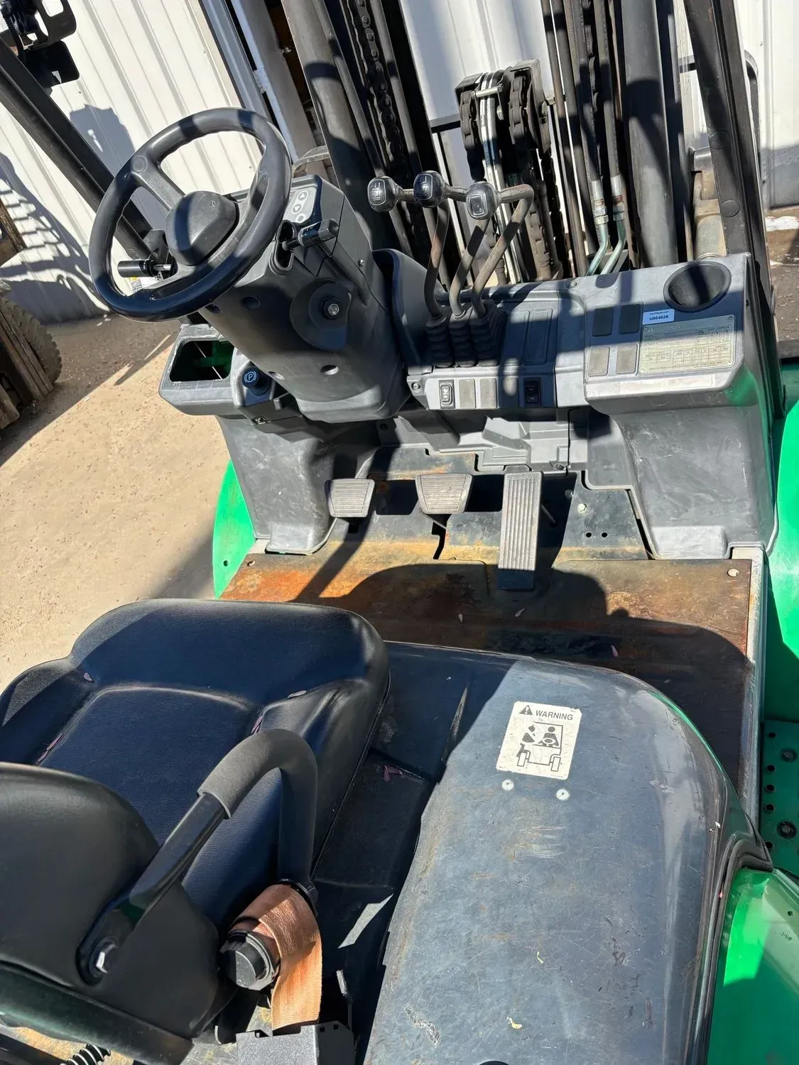 Forklift cab interior with steering wheel, pedals, seat, and controls. Green and black.
