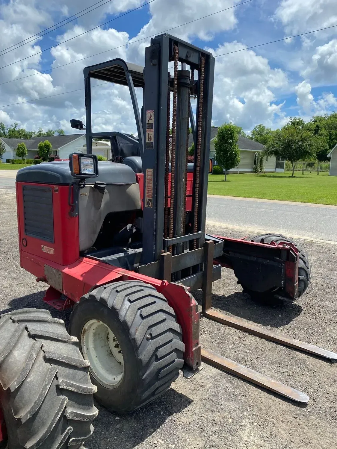 Red and black forklift with large tires on gravel, outdoors.