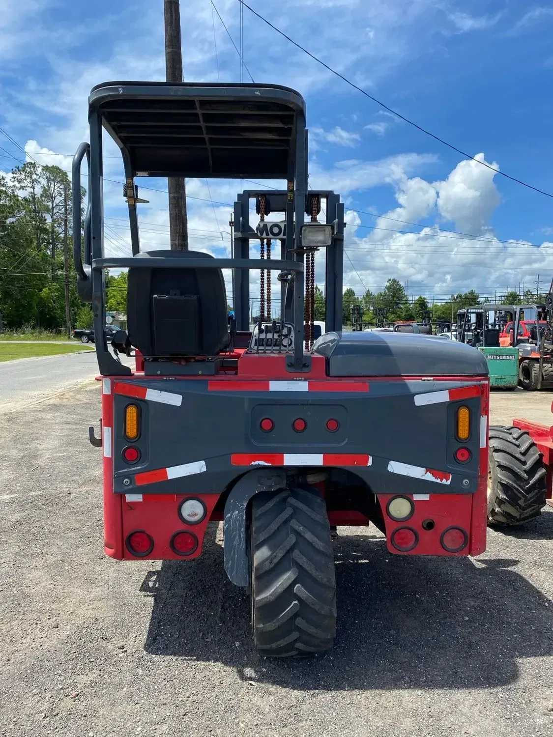 Red and gray forklift with a large front tire, parked on gravel.