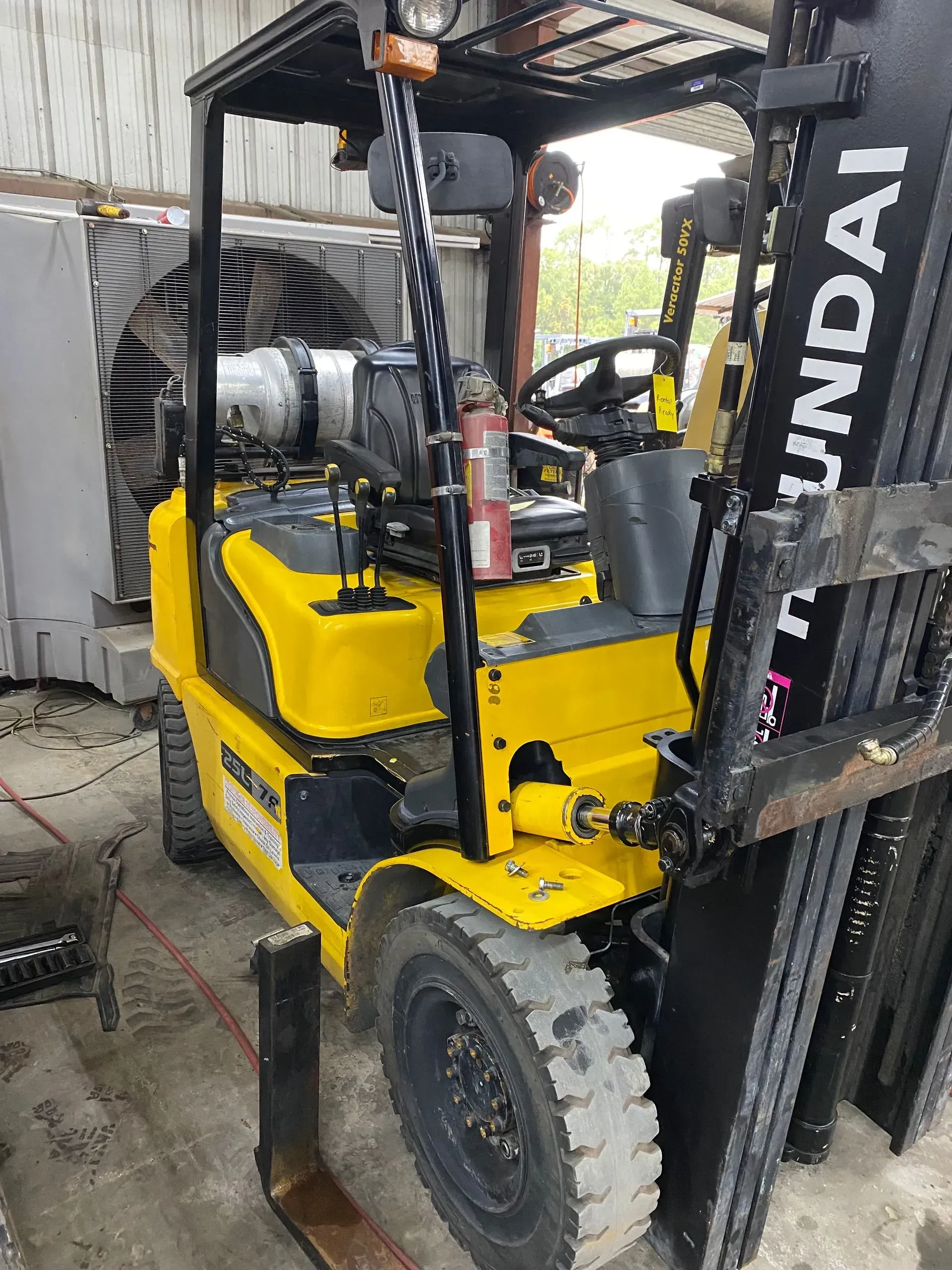 Yellow Hyundai forklift with black forks, a propane tank, and a fire extinguisher, parked indoors.