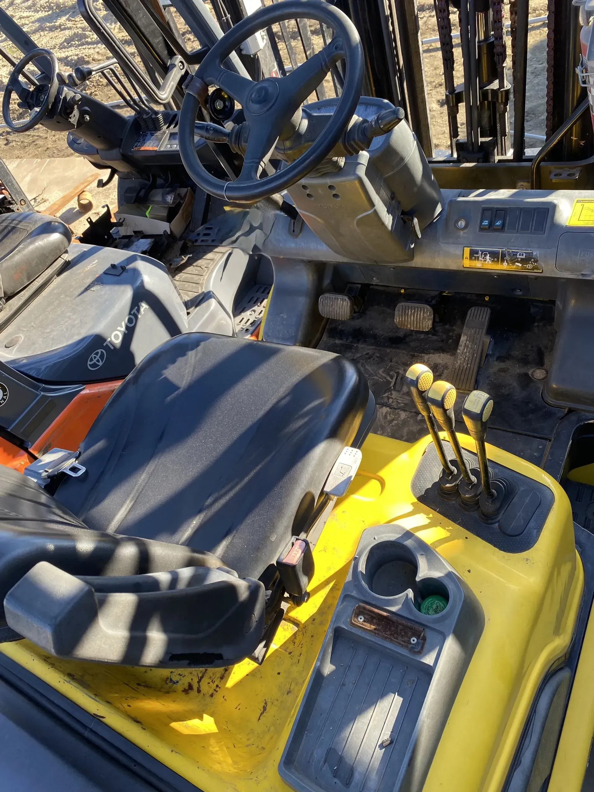 Yellow forklift interior with black seat, steering wheel, and control levers.