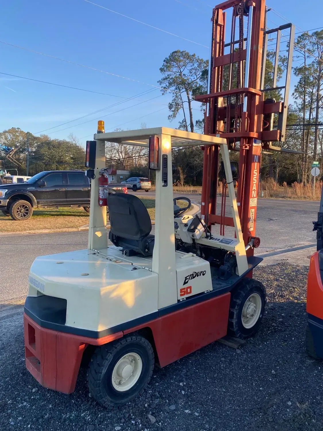 Tan and red forklift in an outdoor lot, mast raised high.
