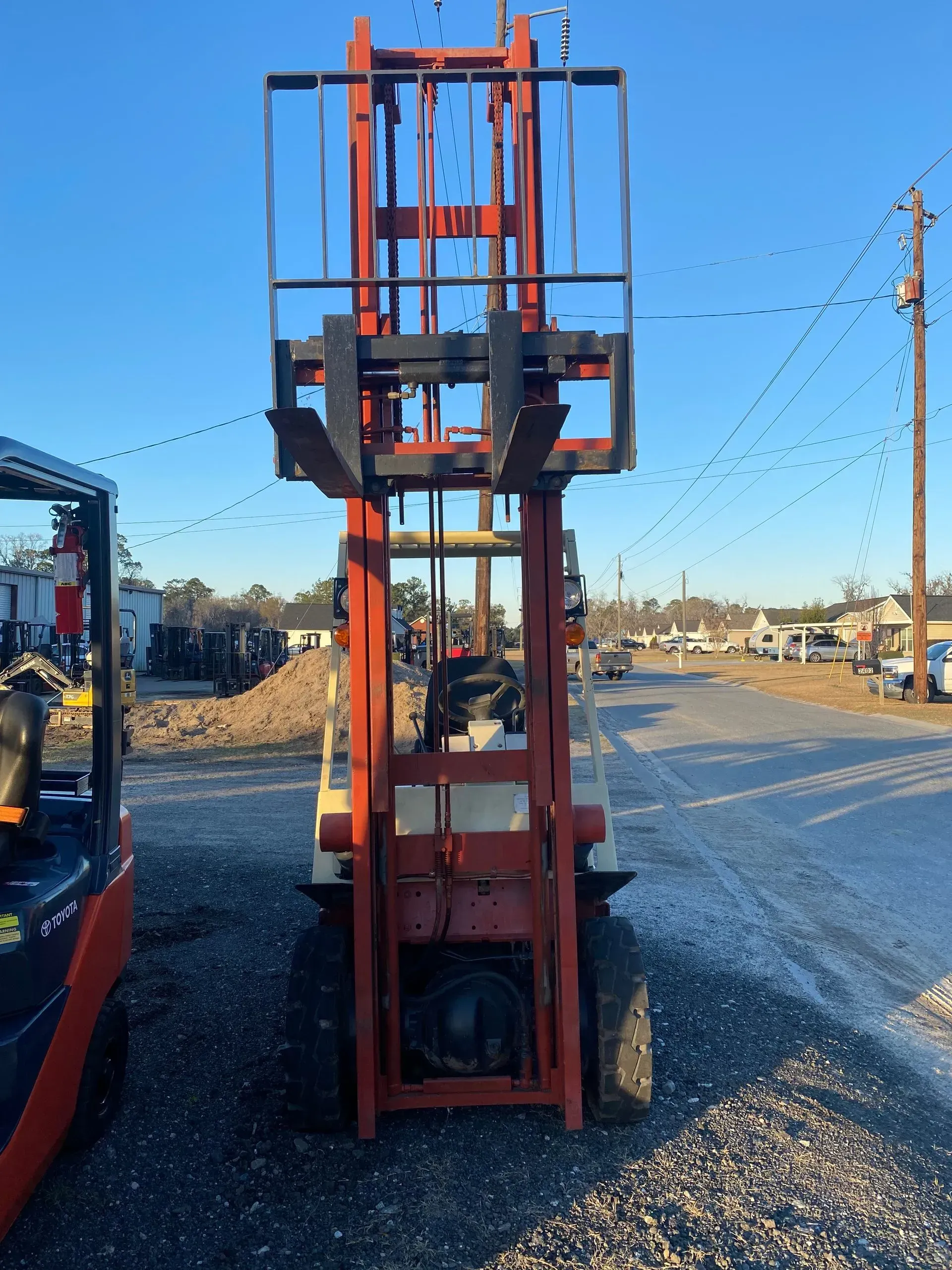 Red and beige forklift in outdoor setting, with raised forks and a metal cage above.