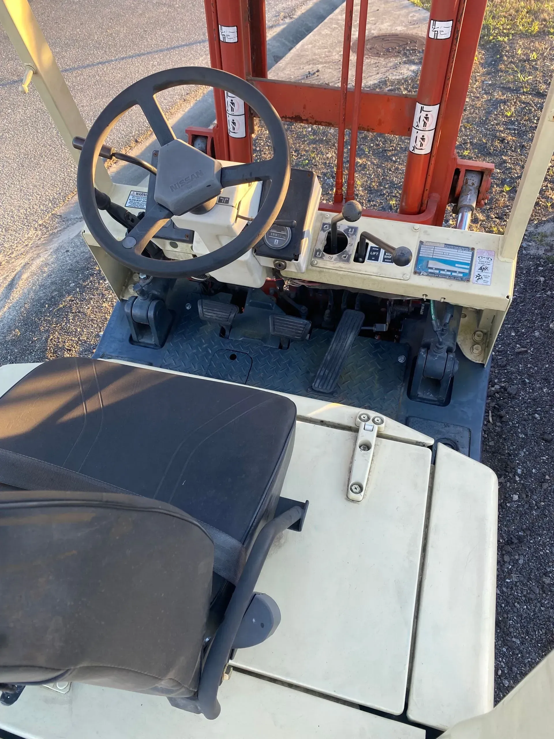 Forklift cockpit with steering wheel, pedals, and seat; orange and cream color scheme.