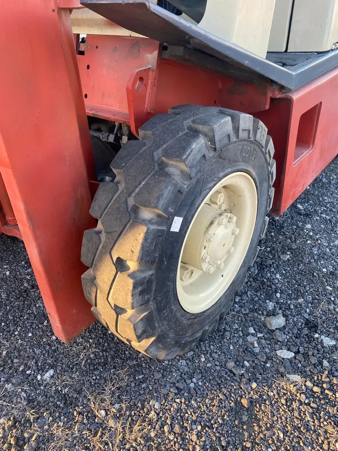 Close-up of a forklift tire with a beige wheel on a gravel surface. The forklift is red.