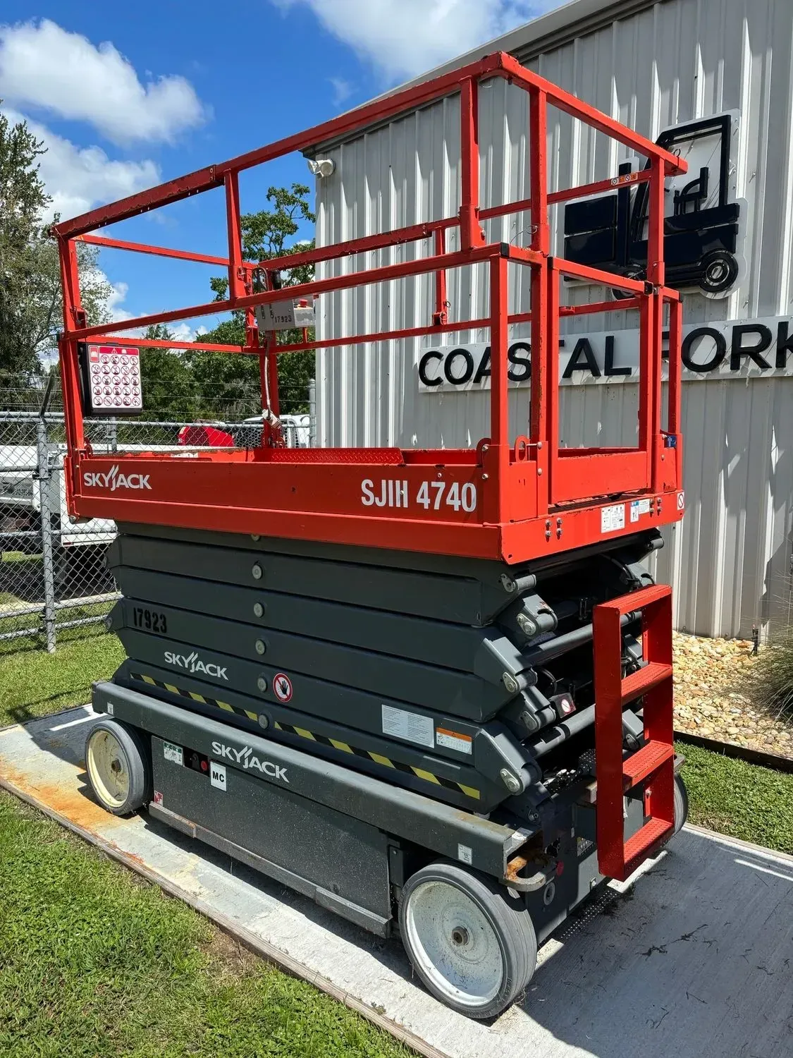 Red and grey Skyjack SJIII 4740 scissor lift outdoors, near a building.
