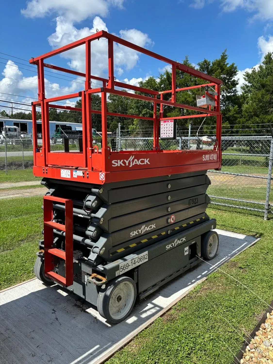 Red and gray Skyjack scissor lift on a concrete slab, outdoors.