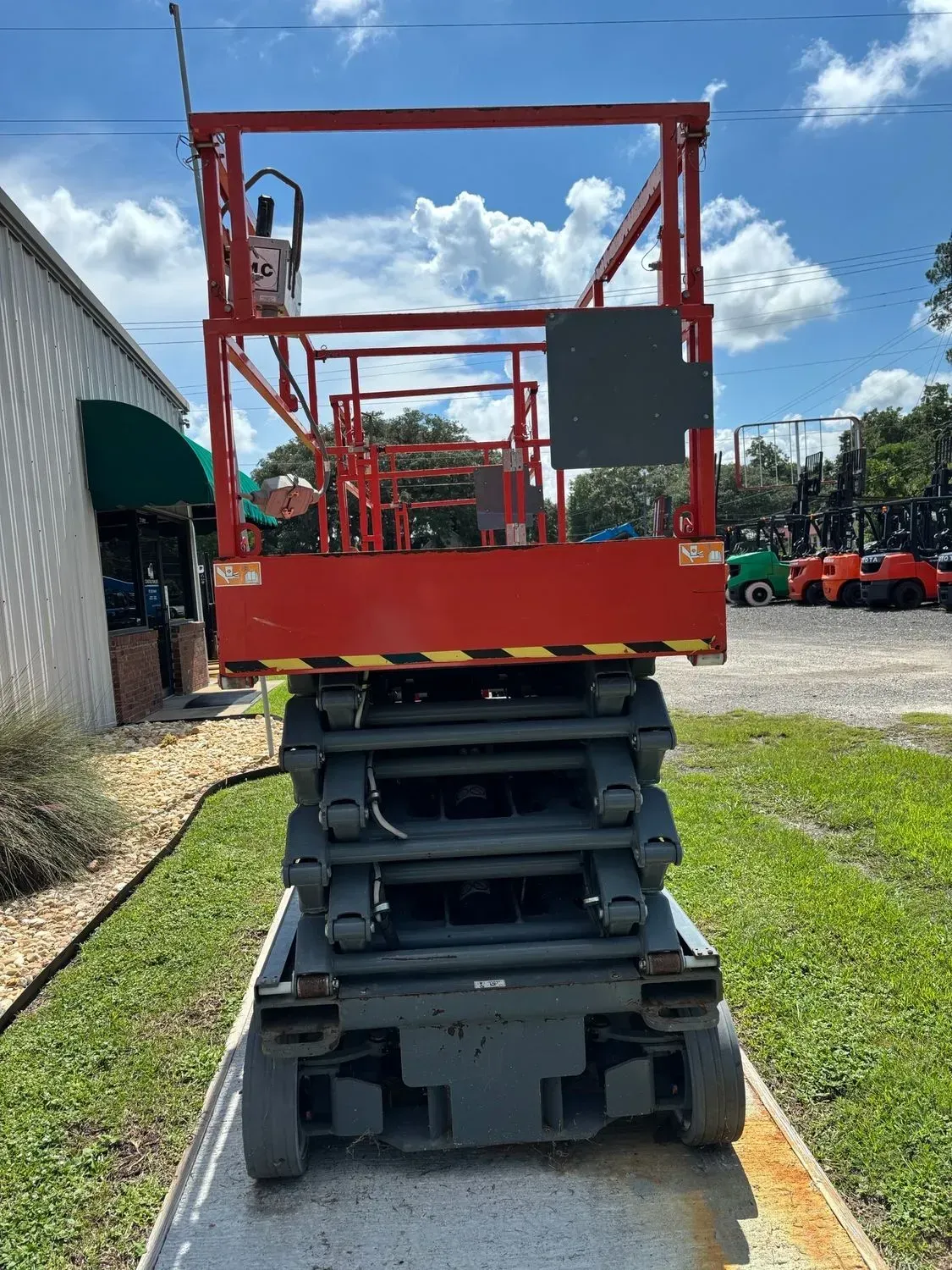 Red and gray scissor lift on a concrete slab in front of a building and a blue sky.