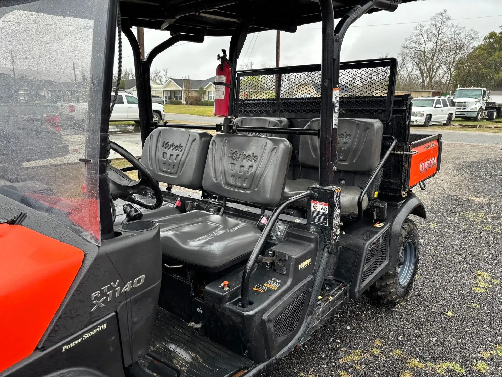 Side view of a Kubota utility vehicle with gray seats, orange accents, and a black roof, parked outdoors.