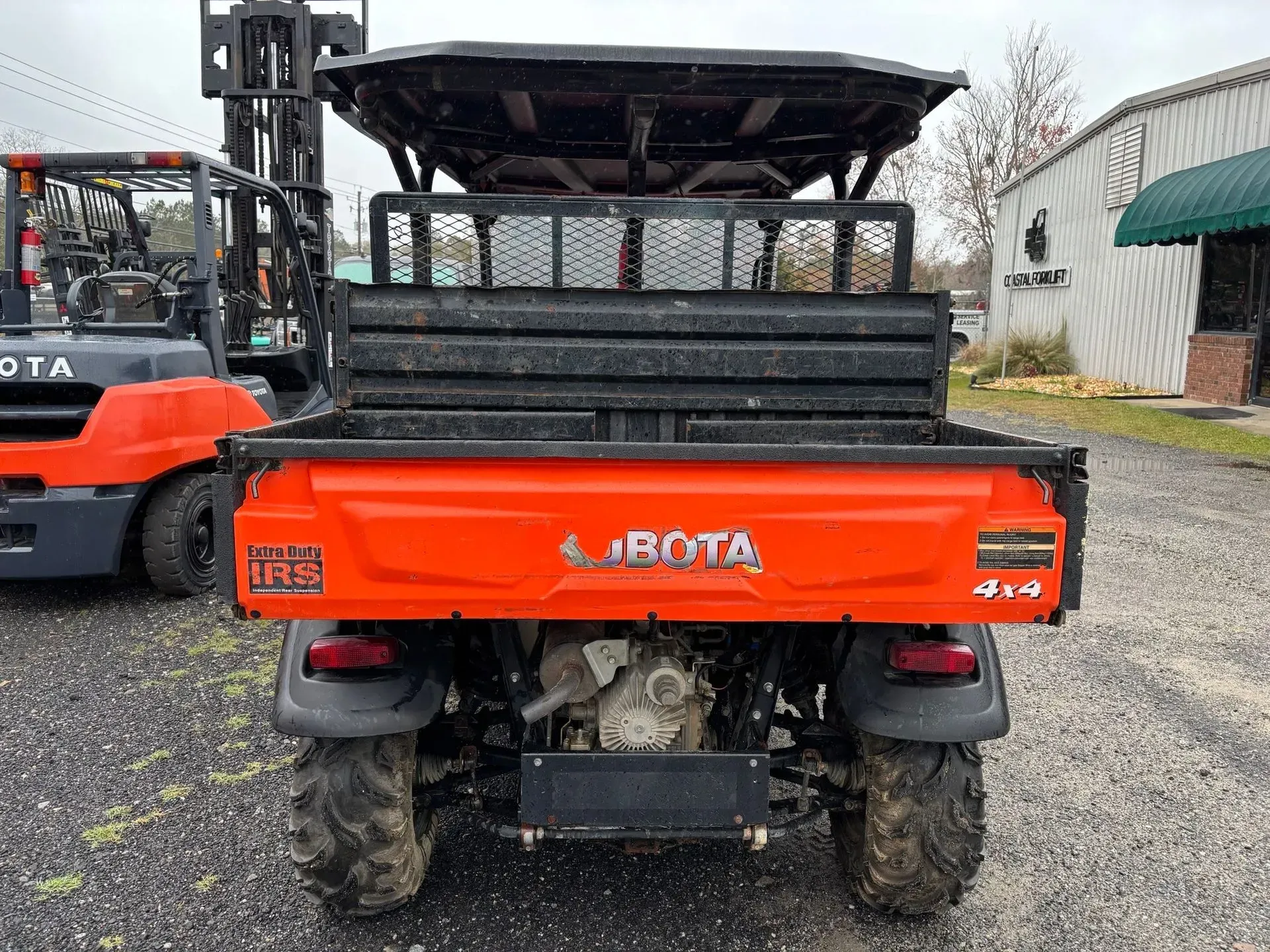 Rear view of a Kubota utility vehicle with an orange bed, 4x4. A forklift is to the left.