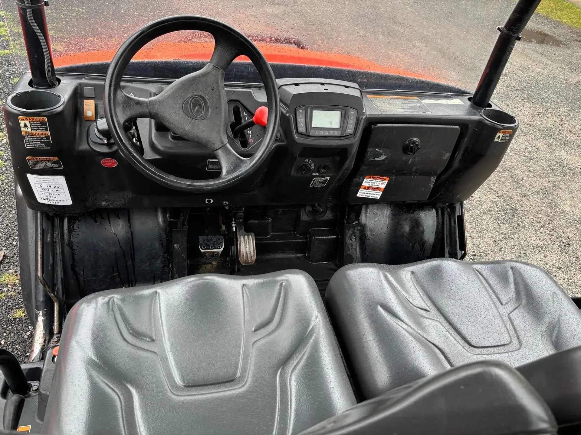 Interior view of an orange utility vehicle. Black dashboard, steering wheel, seats, and cup holders.