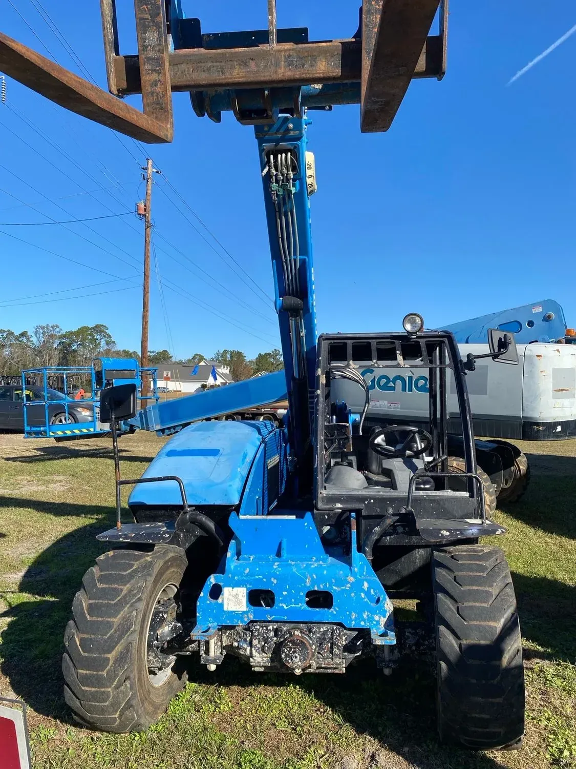 Blue Genie telehandler with forks extended, parked outdoors.