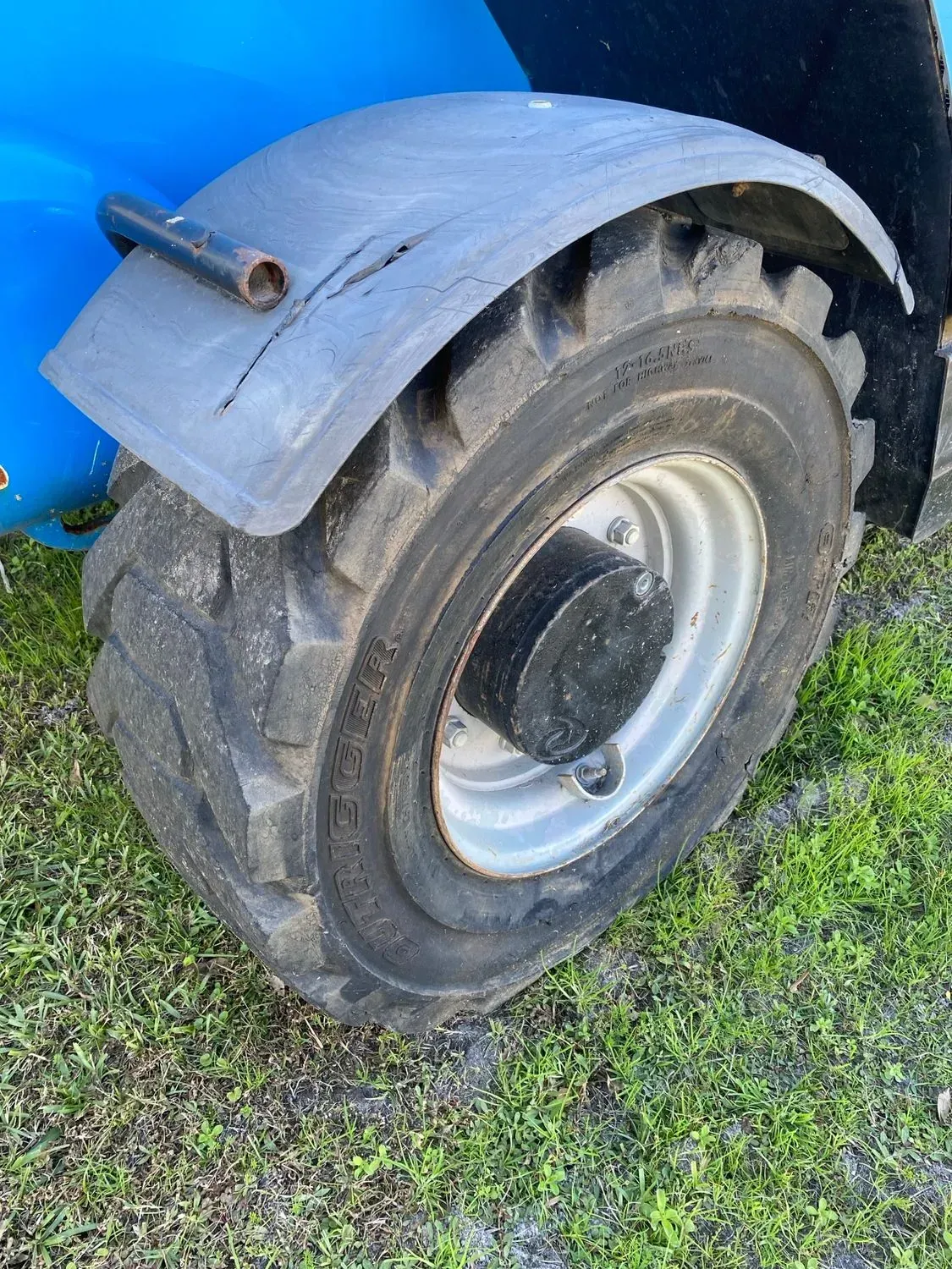 Black tire on a Genie lift with a dark gray fender. The tire is on grass.