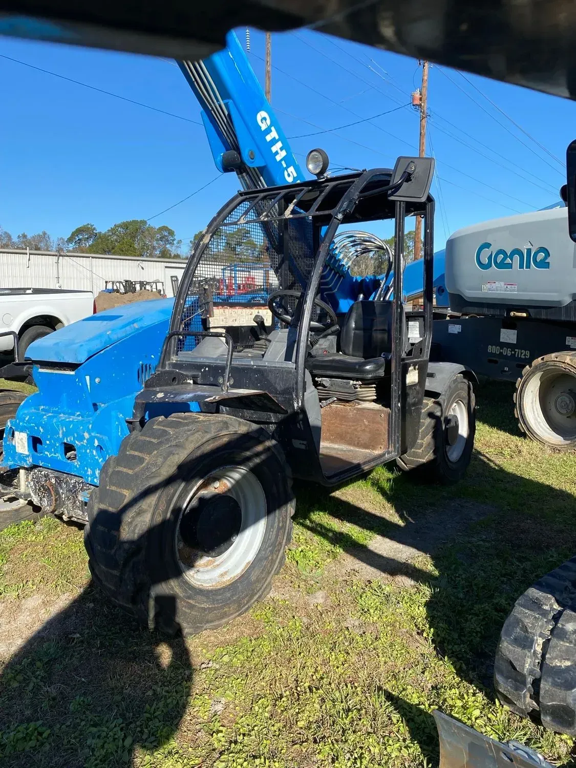 Blue Genie telehandler with raised boom, parked outdoors on grass.