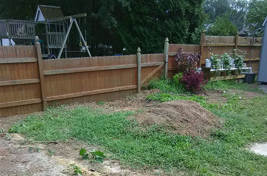 A wooden fence surrounds a backyard with a swing set in the background.
