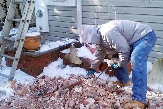 A man is working on a brick chimney in the snow.