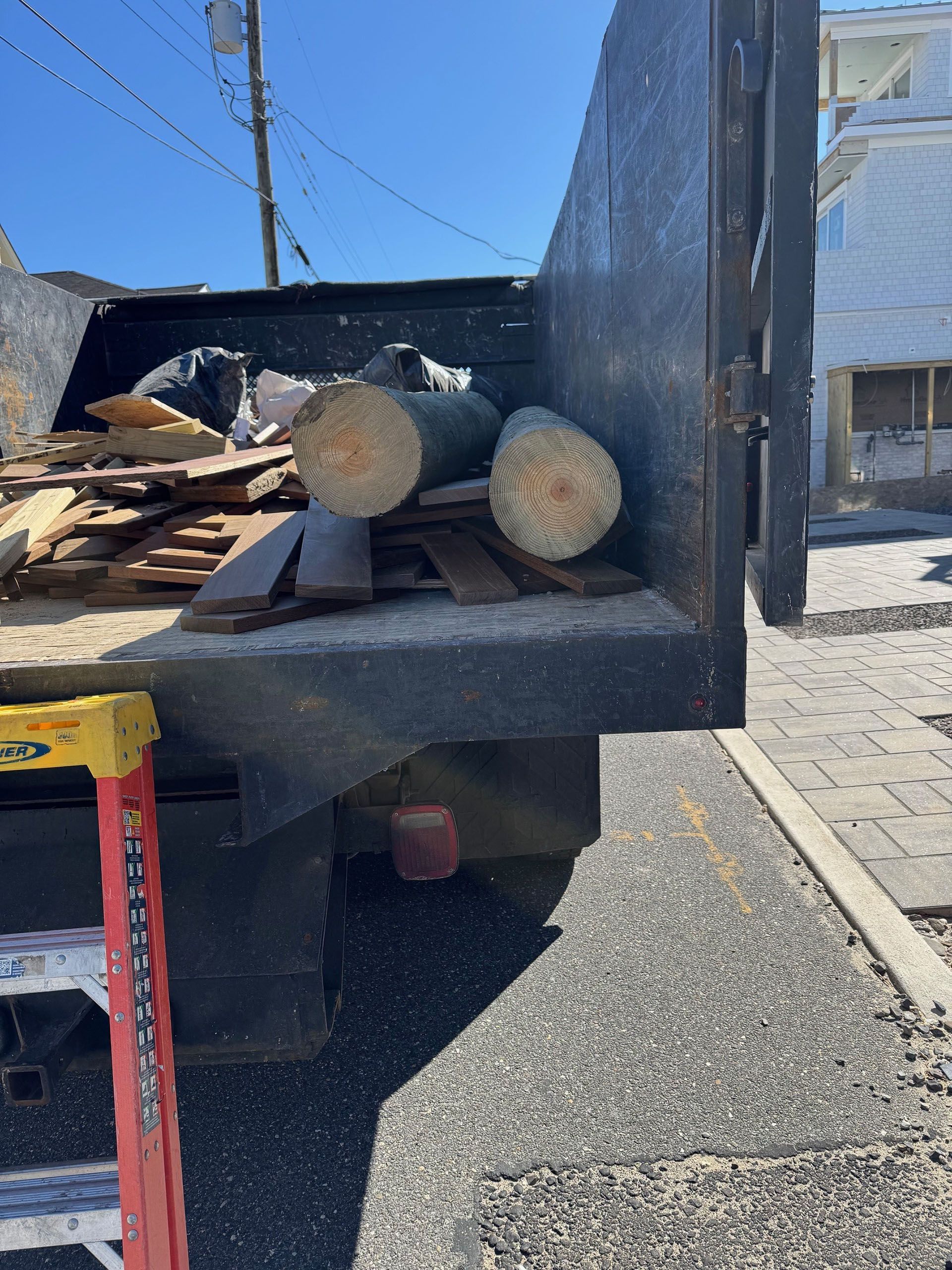 The back of a dump truck filled with logs and a ladder.