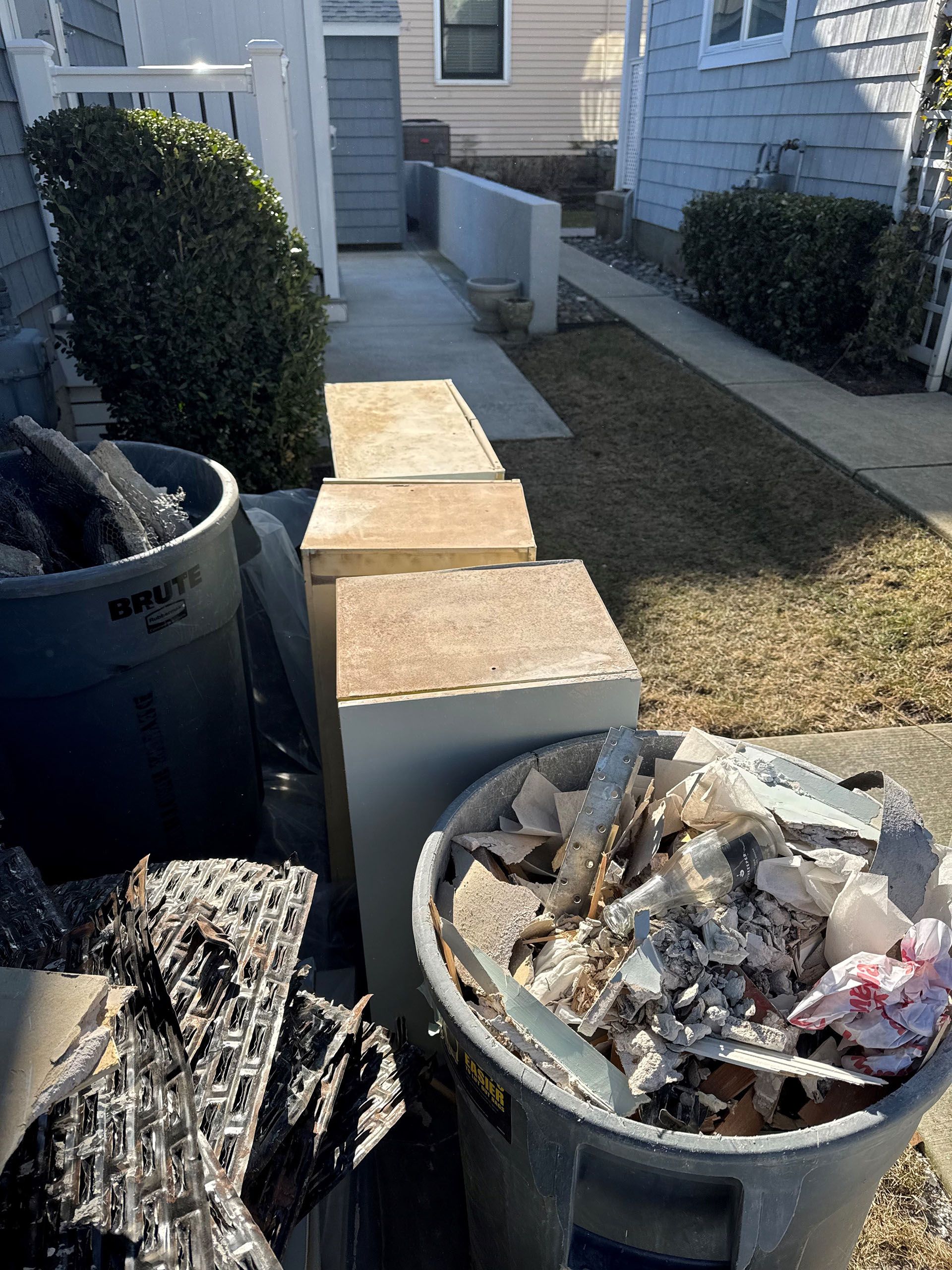 A trash can filled with trash is sitting on the sidewalk in front of a house.