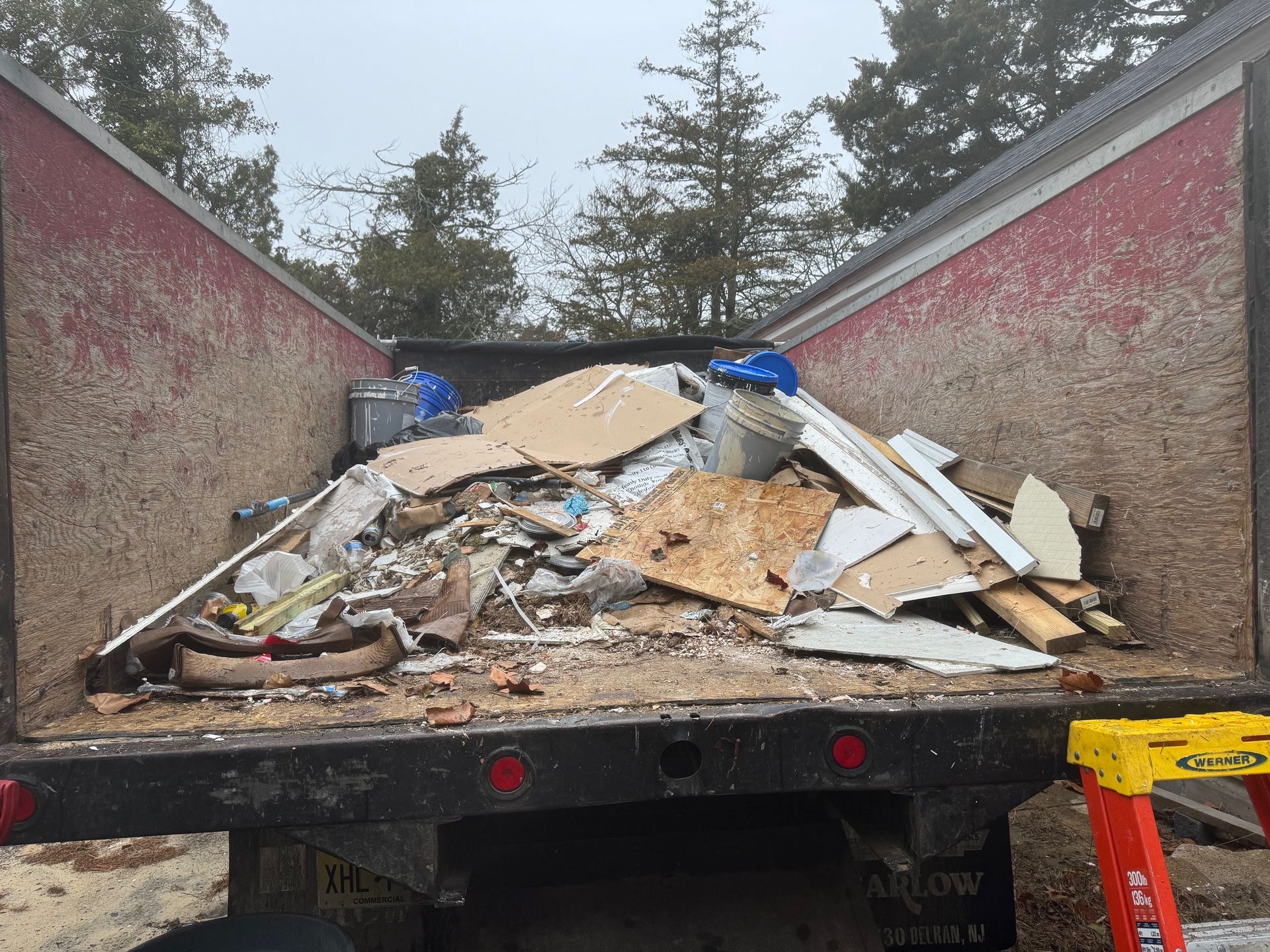 The back of a dumpster filled with junk and a yellow ladder.