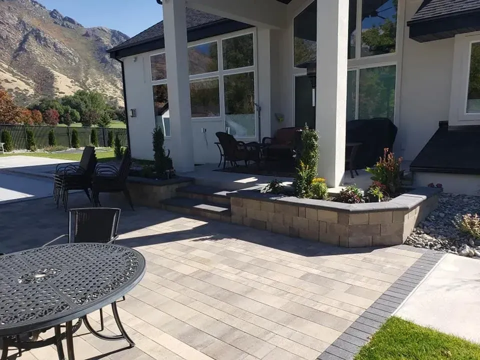 A patio with a table and chairs in front of a house with mountains in the background.