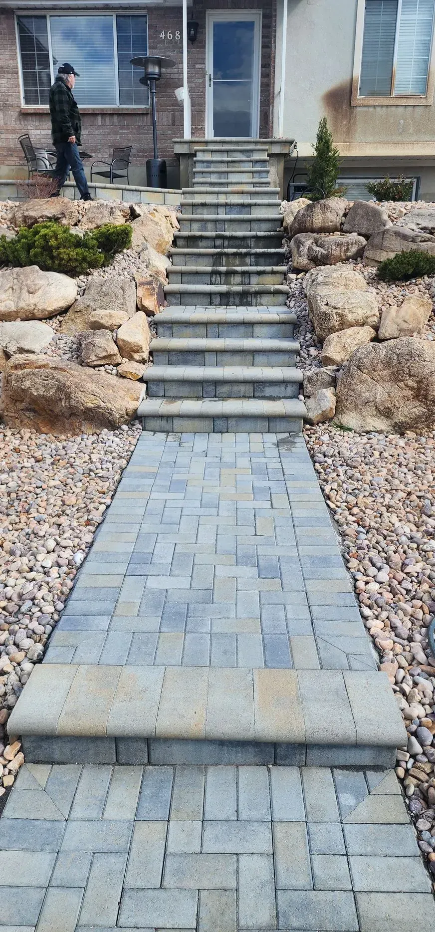 A man is walking down a stone walkway with stairs leading up to a house.