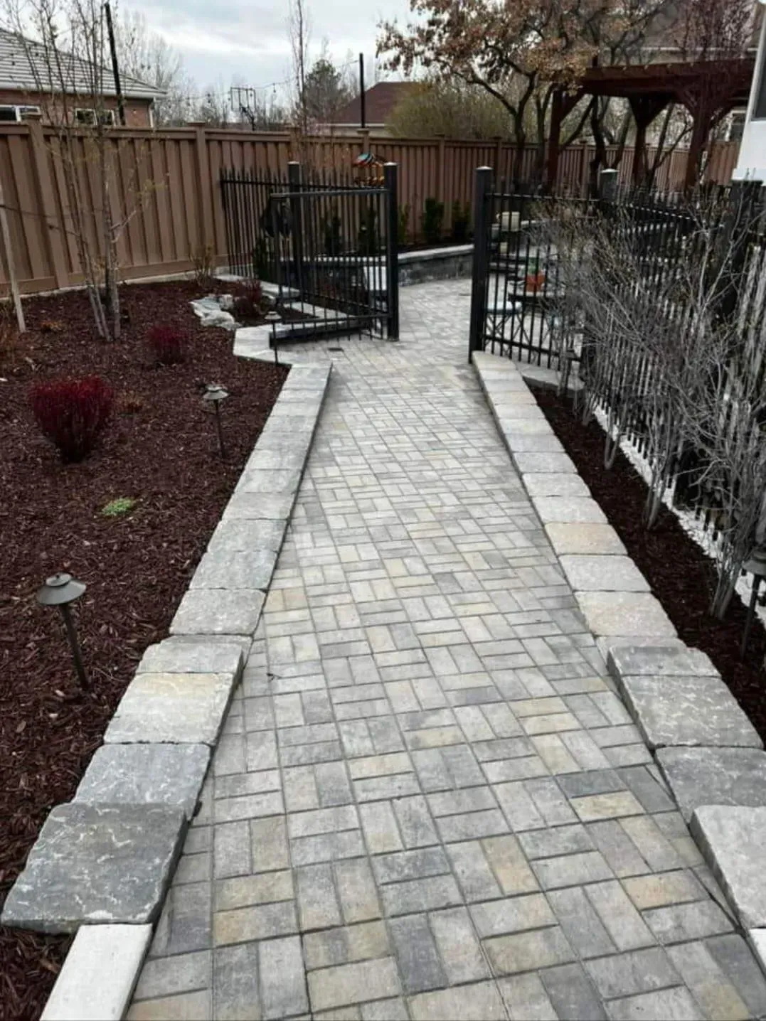 A brick walkway leading to a gate in a backyard.