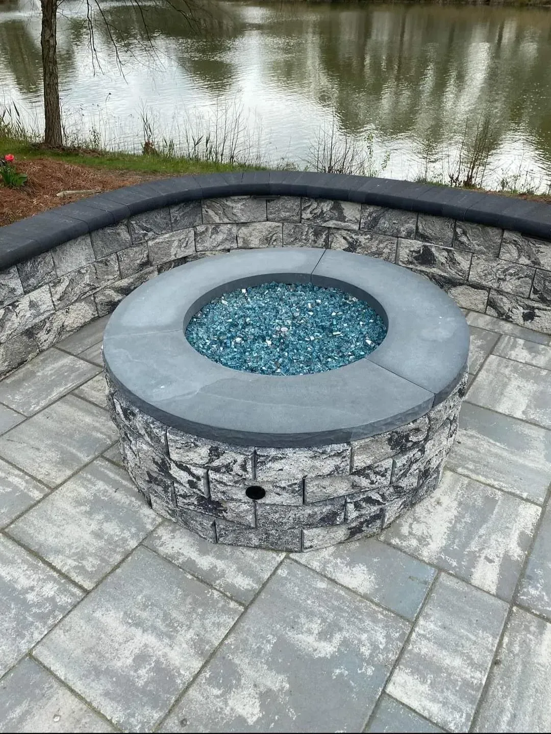 A fire pit is sitting on a patio next to a lake.